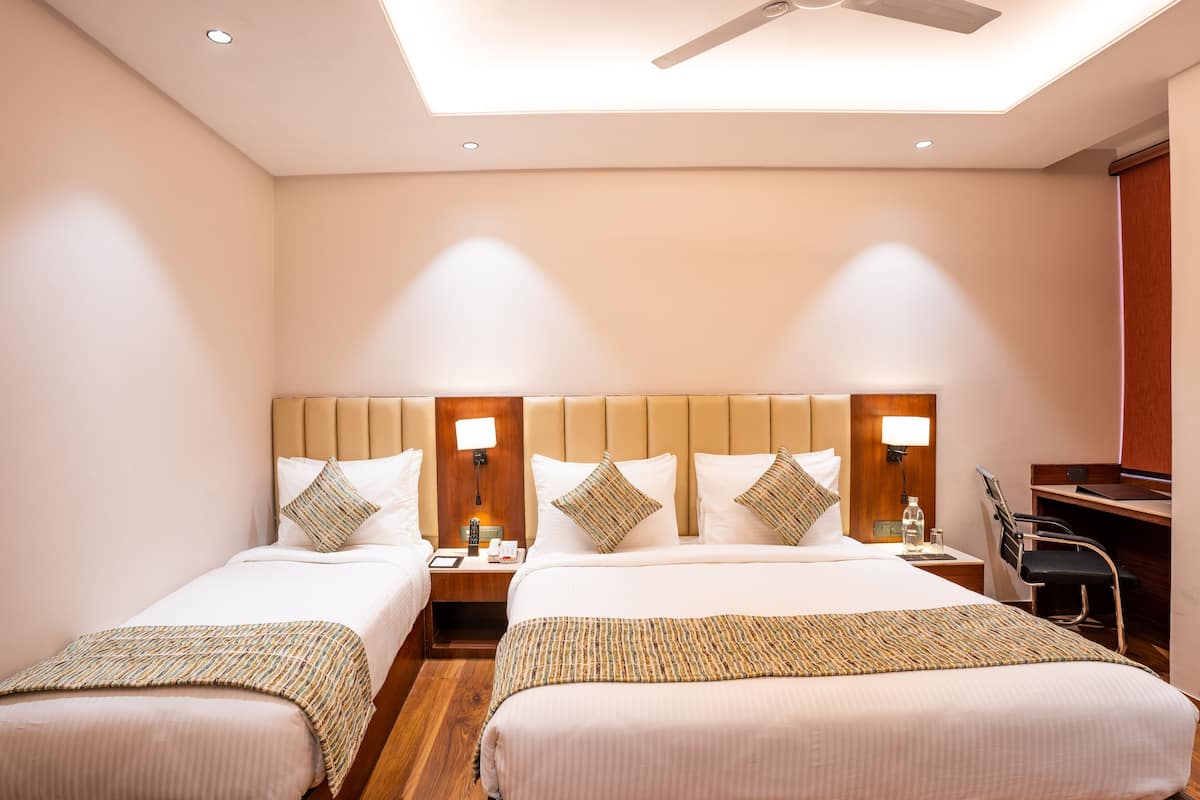 A hotel room with two beds, a desk, and a chair. There are nightstands with lamps and a ceiling fan.