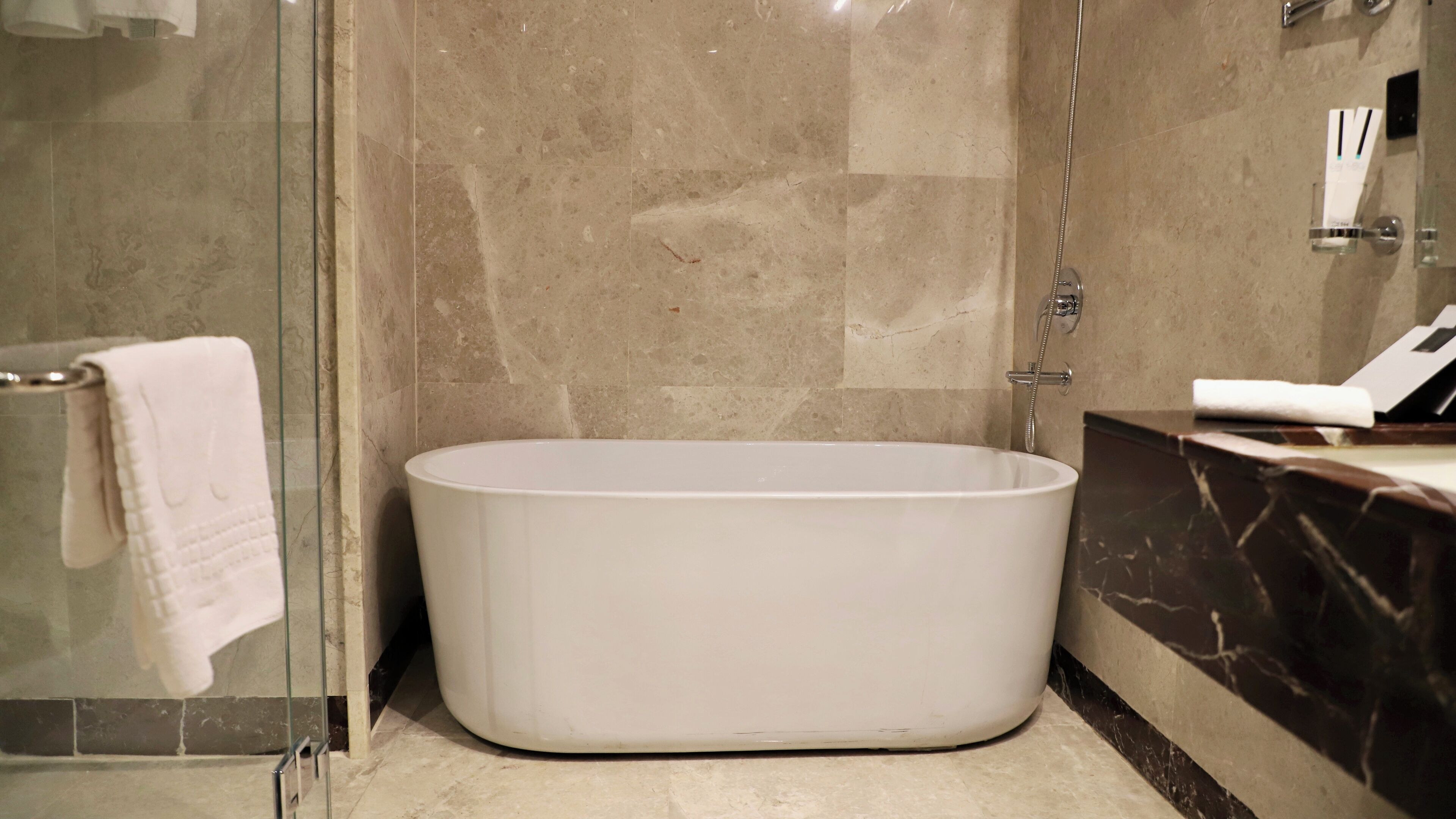 Un baño moderno con una bañera independiente, una cabina de ducha con mampara de vidrio y un revestimiento de mármol en la pared.