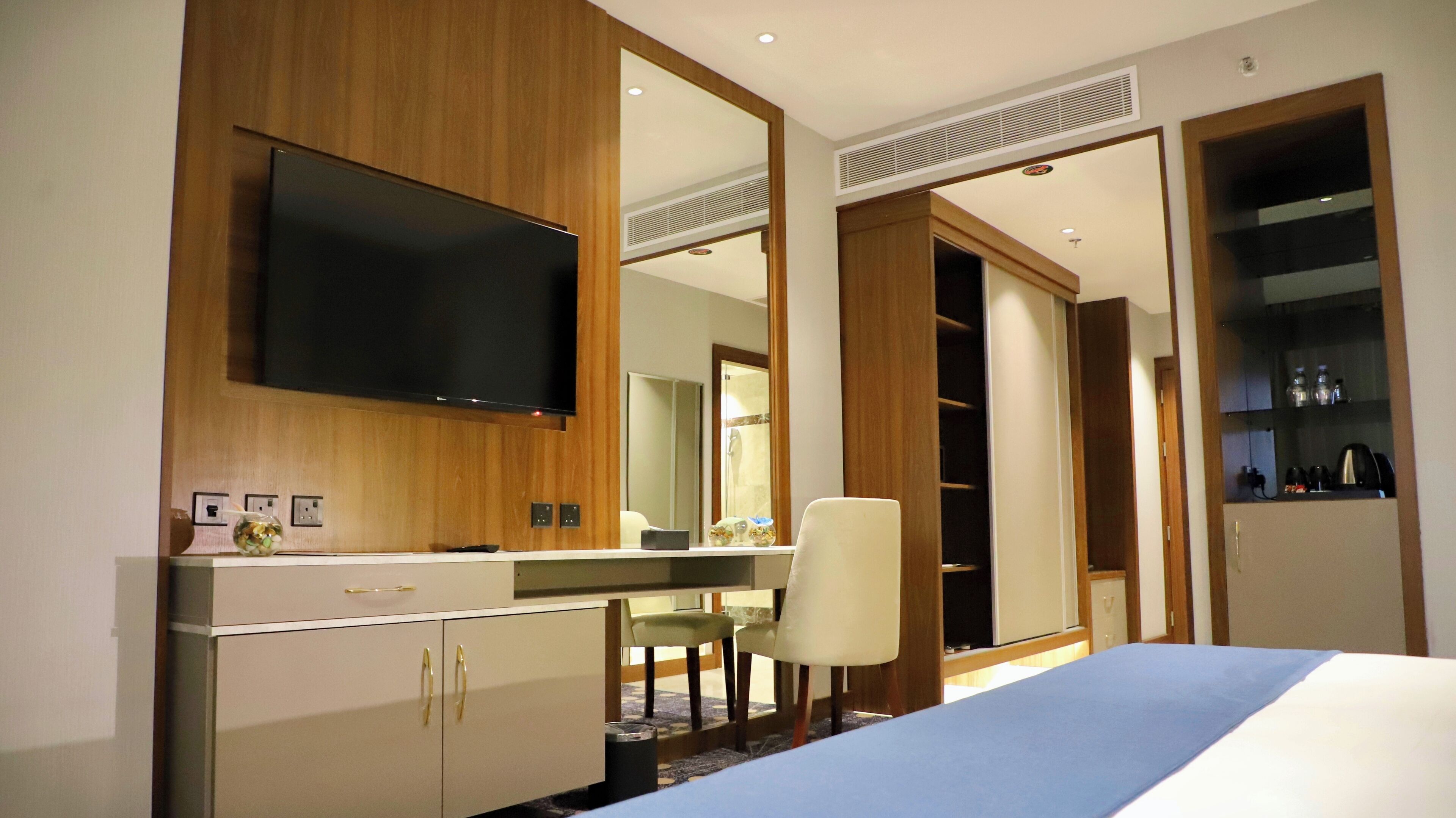 A hotel room with a bed, a desk, a chair, a TV, a wardrobe, and a bathroom mirror.