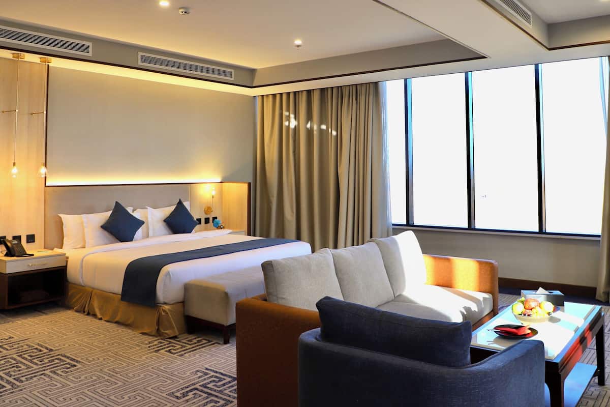 A hotel room with a large bed, a desk, a chair, and a window with curtains.