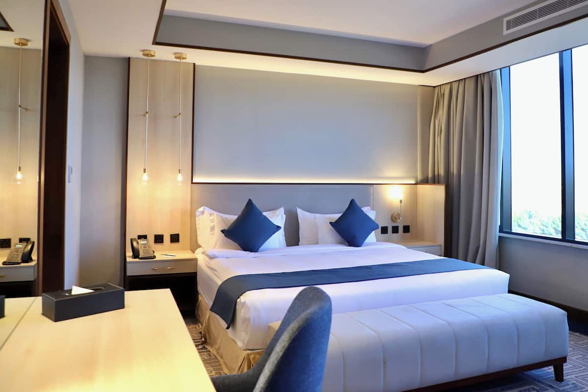 A hotel room with a large bed, a desk, a phone, and a window with curtains.
