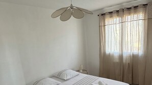 Un dormitorio con una cama grande, ventilador de techo, mesita de noche y ventana con cortinas.