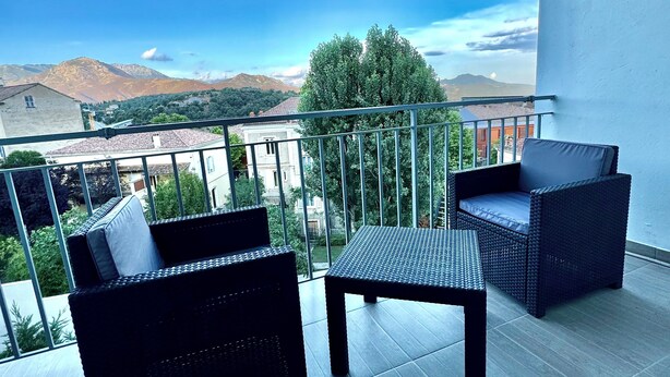 Un balcón con mobiliario de mimbre, una mesa y vistas a montañas y vegetación.