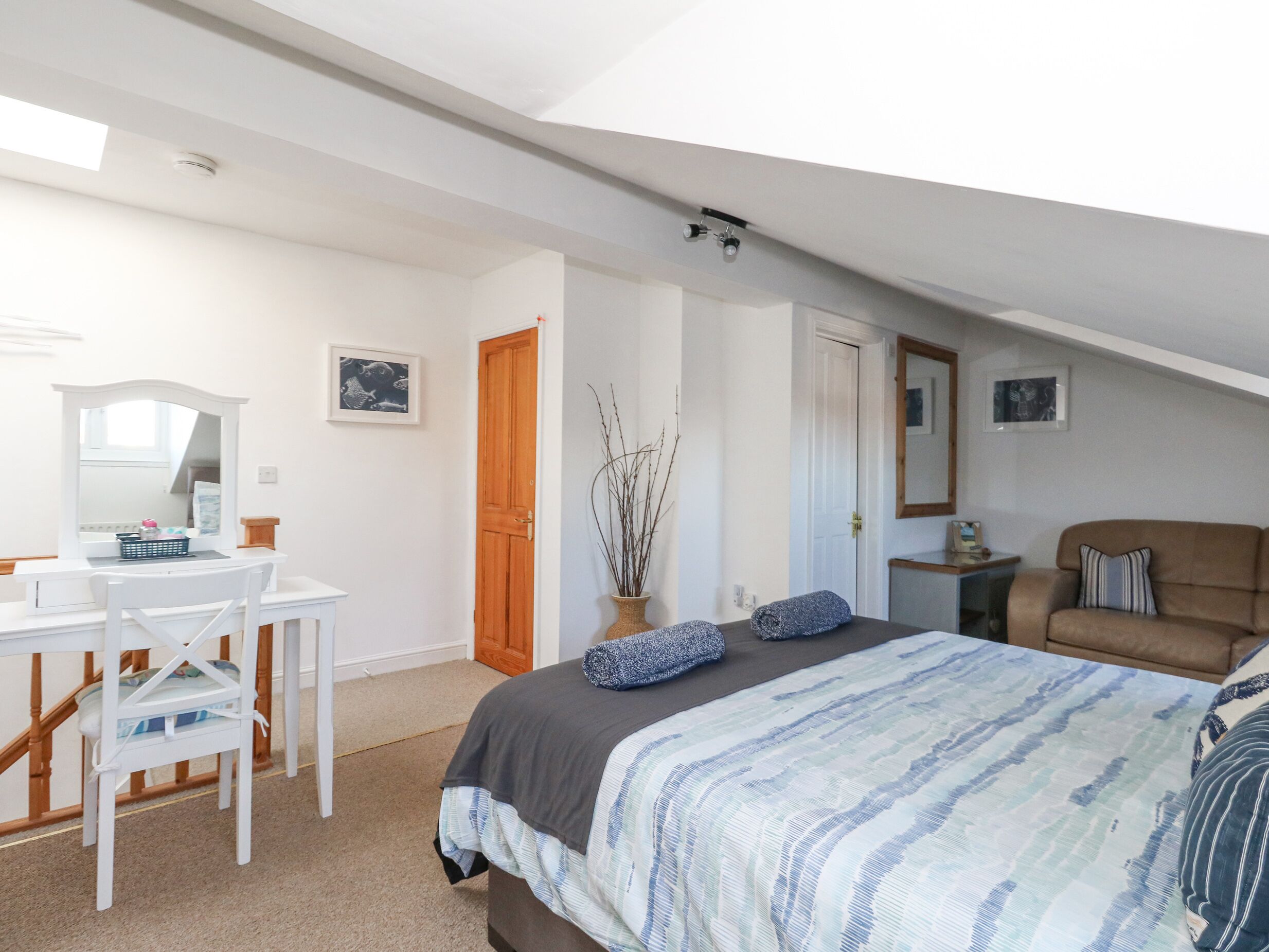 A bedroom with a bed, a desk, a chair, a dresser, a mirror, and a door.