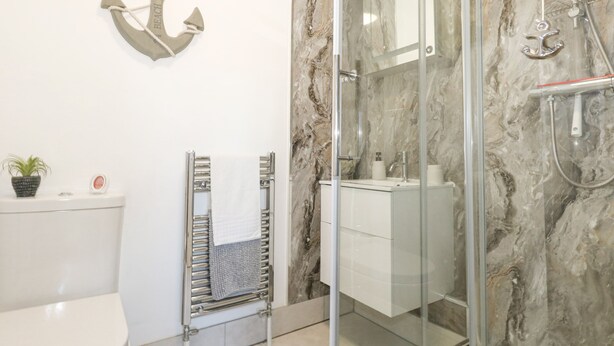 Une salle de bain moderne dotée d’une douche à parois de verre, d’un pare-baignoire en marbre et de toilettes avec un sèche-serviettes.