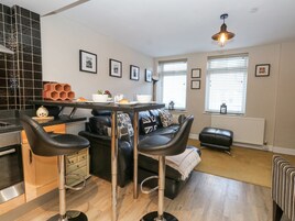 Una cocina moderna con zona de comedor, que incluye un sofá de cuero negro, dos taburetes de bar y una mesa preparada para dos personas.