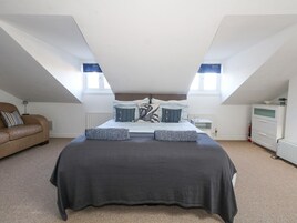 Un dormitorio con una cama grande, dos ventanas, un radiador, un aparador y un sofá de cuero marrón.