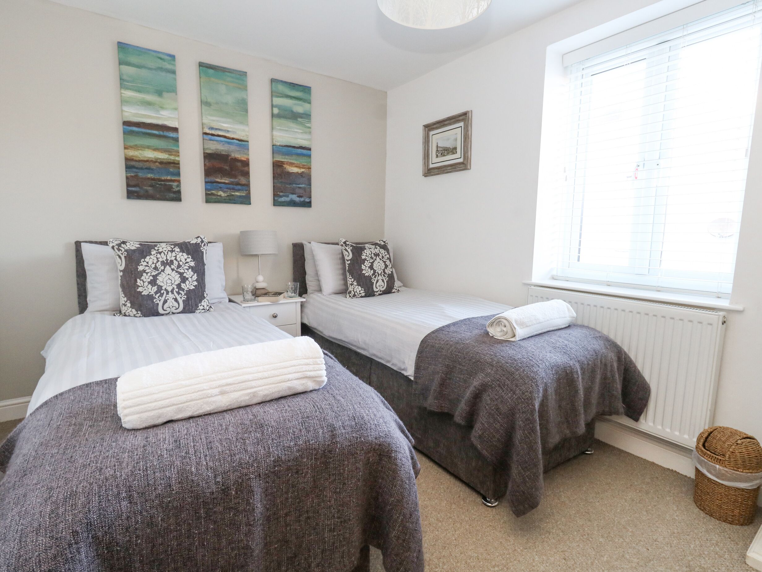 A bedroom with two beds, a nightstand, a lamp, a framed picture, and a window with blinds.