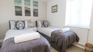 A bedroom with two beds, a nightstand, a lamp, a framed picture, and a window with blinds.