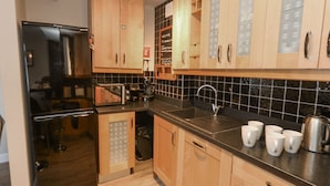 A modern kitchen with wooden cabinets, a black tiled backsplash, stainless steel appliances, and a coffee station. - Anchor Cottage (Weymouth)