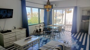 A room with a bed, a TV, a dining table with chairs, a small kitchen area, and a view of the outside. - Magnificent S+1 with panoramic view of Port El Kantaoui (Hammam Sousse)