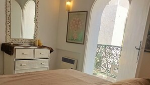 A bedroom with a large bed, a dresser, a mirror, and a window with an arched view. - Magnificent S+1 with panoramic view of Port El Kantaoui (Hammam Sousse)