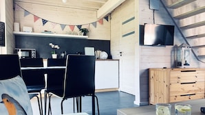 Una cocina moderna con microondas, cafetera y una pequeña planta. Hay una zona de comedor con mesa y sillas, y un mueble de madera con cajones.