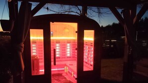 Una sauna con revestimiento de madera y puertas de vidrio, que incluye un banco y suelo de baldosas en su interior.