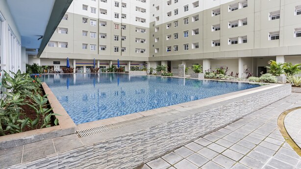 A swimming pool surrounded by a stone-tiled deck, with a multi-story building in the background. - Capital O 93593 Pelangi Loftville City (South Tangerang)