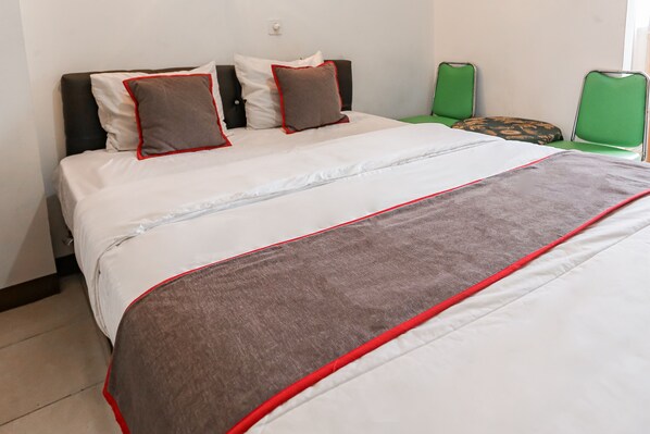 A neatly made bed with white and brown bedding, a red accent, and two green chairs against the wall.