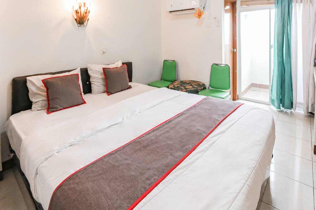 Ein Hotelzimmer mit einem großen Bett, grünen Sesseln, einem kleinen Tisch und Blick ins Freie.