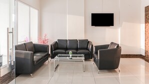 A modern living room with a glass coffee table, two black leather sofas, and a flat-screen TV mounted on the wall. - Capital O 93593 Pelangi Loftville City (South Tangerang)