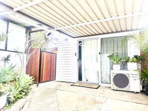 A covered patio area with a sliding glass door, a Panasonic inverter air conditioner, and various potted plants. - Happy Guest house in Newcastle (Mayfield West)