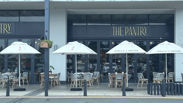 Un espace extérieur aménagé avec des parasols et des chaises en osier, situé devant un bâtiment portant l’inscription « THE PANTRY ».