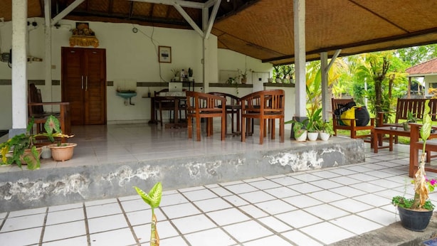 A covered outdoor area with a tiled floor, wooden furniture, and potted plants. - Hotel O Hepi Bungalow Lovina (Buleleng)