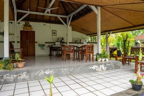 A covered outdoor area with a tiled floor, wooden furniture, and potted plants. - Hotel O Hepi Bungalow Lovina (Buleleng)