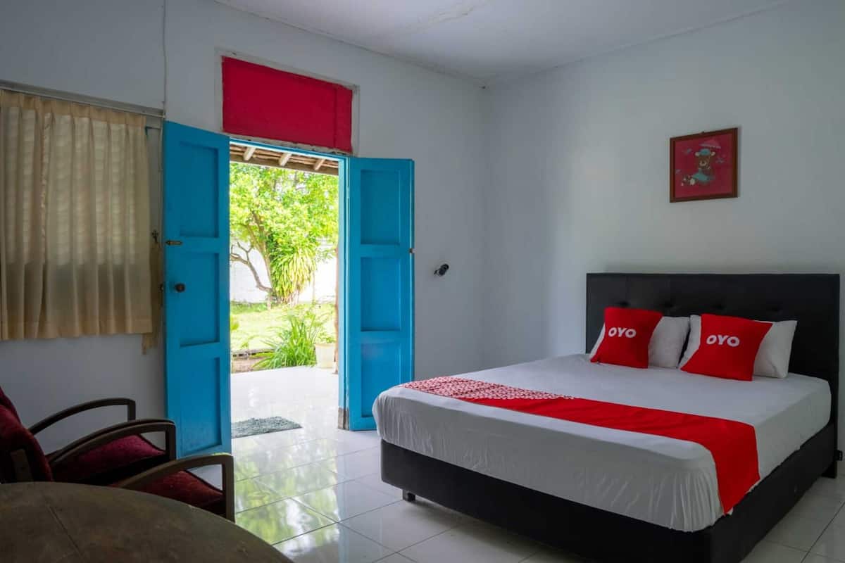 A hotel room with a bed, a chair, a door, and a view of greenery outside.