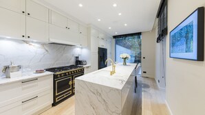 A modern kitchen with white cabinetry, a black stove, and a marble countertop.
