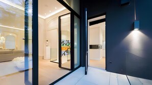A modern interior with a glass door entrance, a seating area with a sofa, and a kitchen visible through the door.