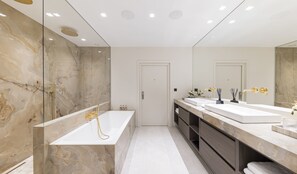 Un baño moderno con un espejo grande, dos lavamanos, una bañera y paredes de mármol.