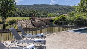 Un espace aménagé au bord de la piscine, avec des chaises longues et une vue sur un bâtiment rustique et des collines.