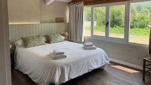 Une chambre avec un grand lit, un plafond en bois et une fenêtre donnant sur un paysage verdoyant.