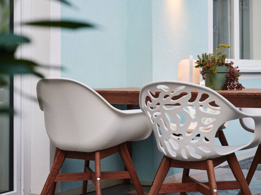 Een moderne buiten zithoek met twee witte stoelen en een tafel, een potplant en een wandlamp.