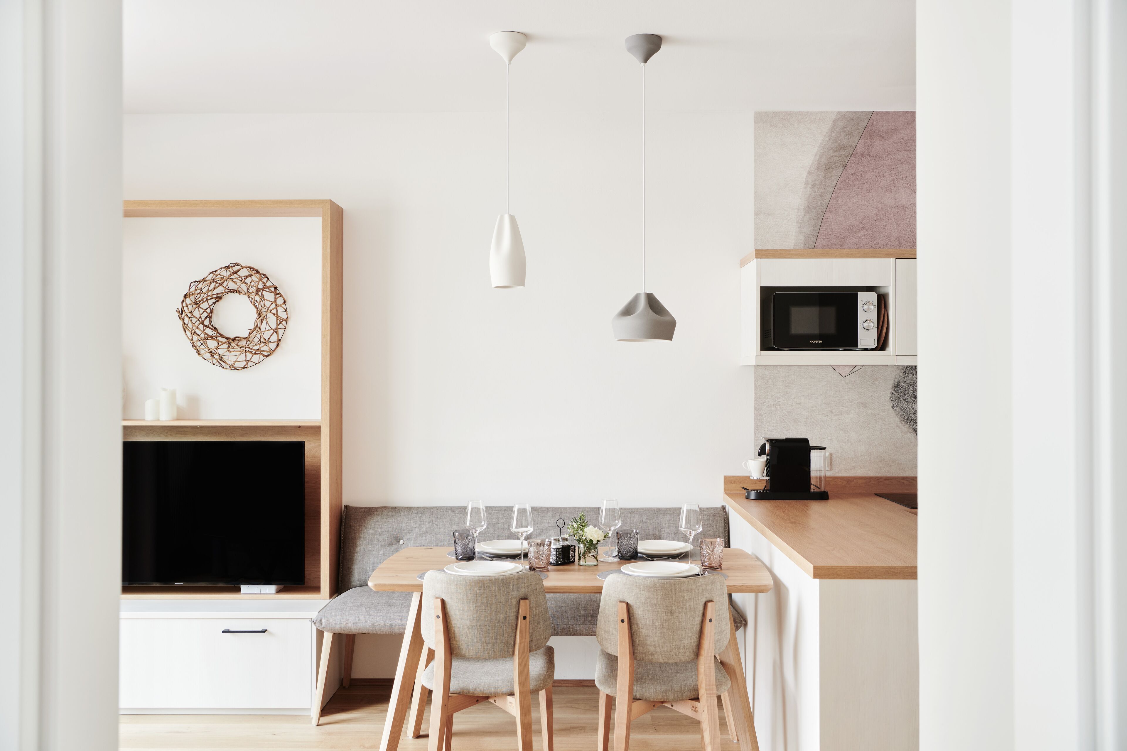 A modern kitchen with a dining table set for two, a microwave, and a television on a wooden cabinet.