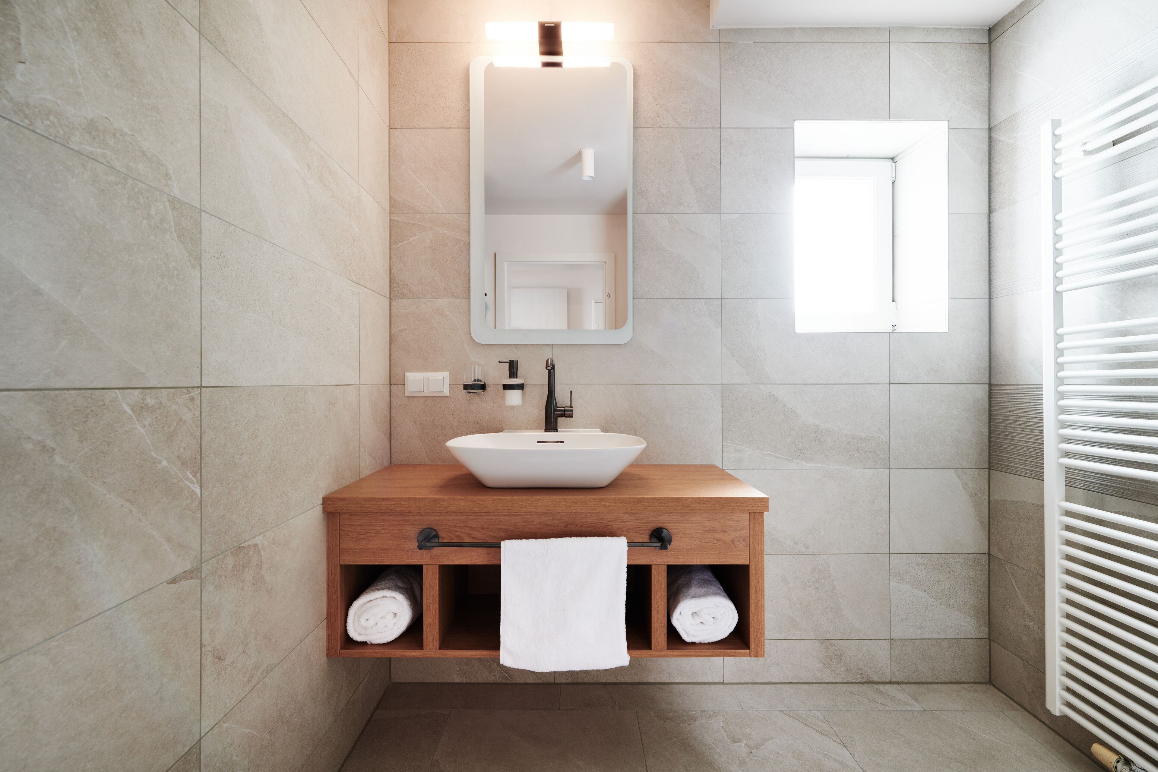 A modern bathroom with a wooden vanity, a white sink, and a towel rack.