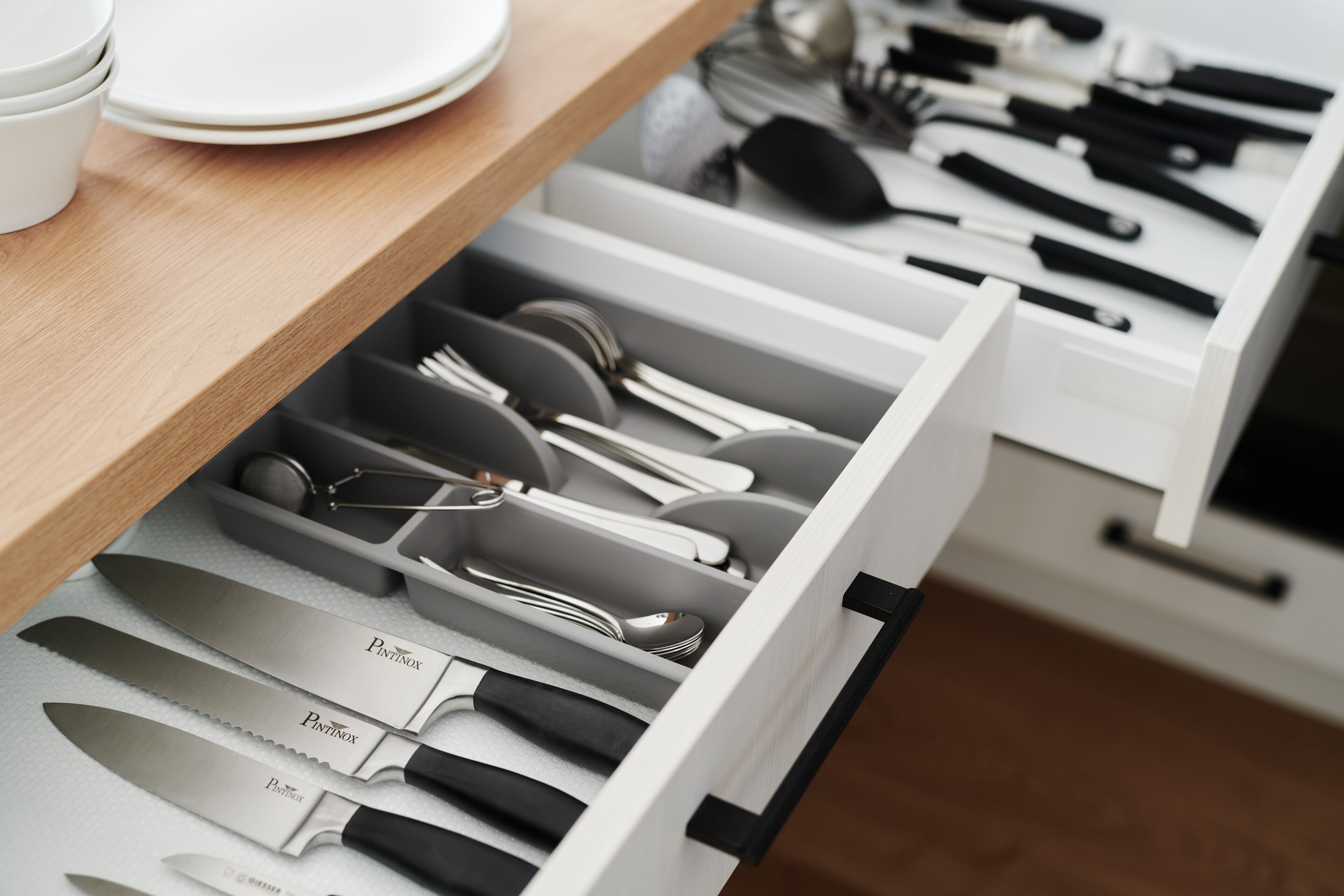 A kitchen drawer with neatly organized utensils and cutlery, including knives, spoons, and forks.