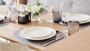 A dining table set with plates, cutlery, and wine glasses, with a vase of flowers and a salt and pepper shaker on the table.