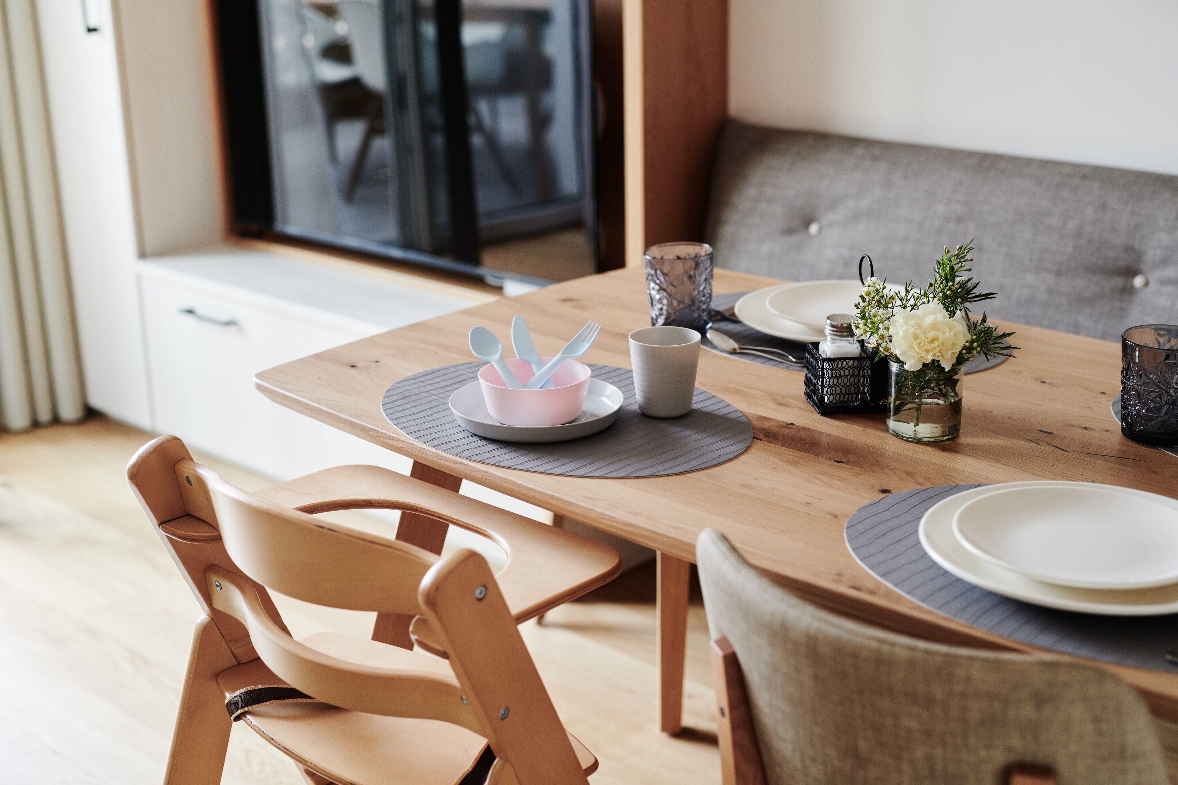 Een eettafel gedekt met borden, bestek en een bloevas.