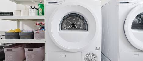 Varias lavadoras blancas con paneles de control y un estante superior con productos de limpieza.
