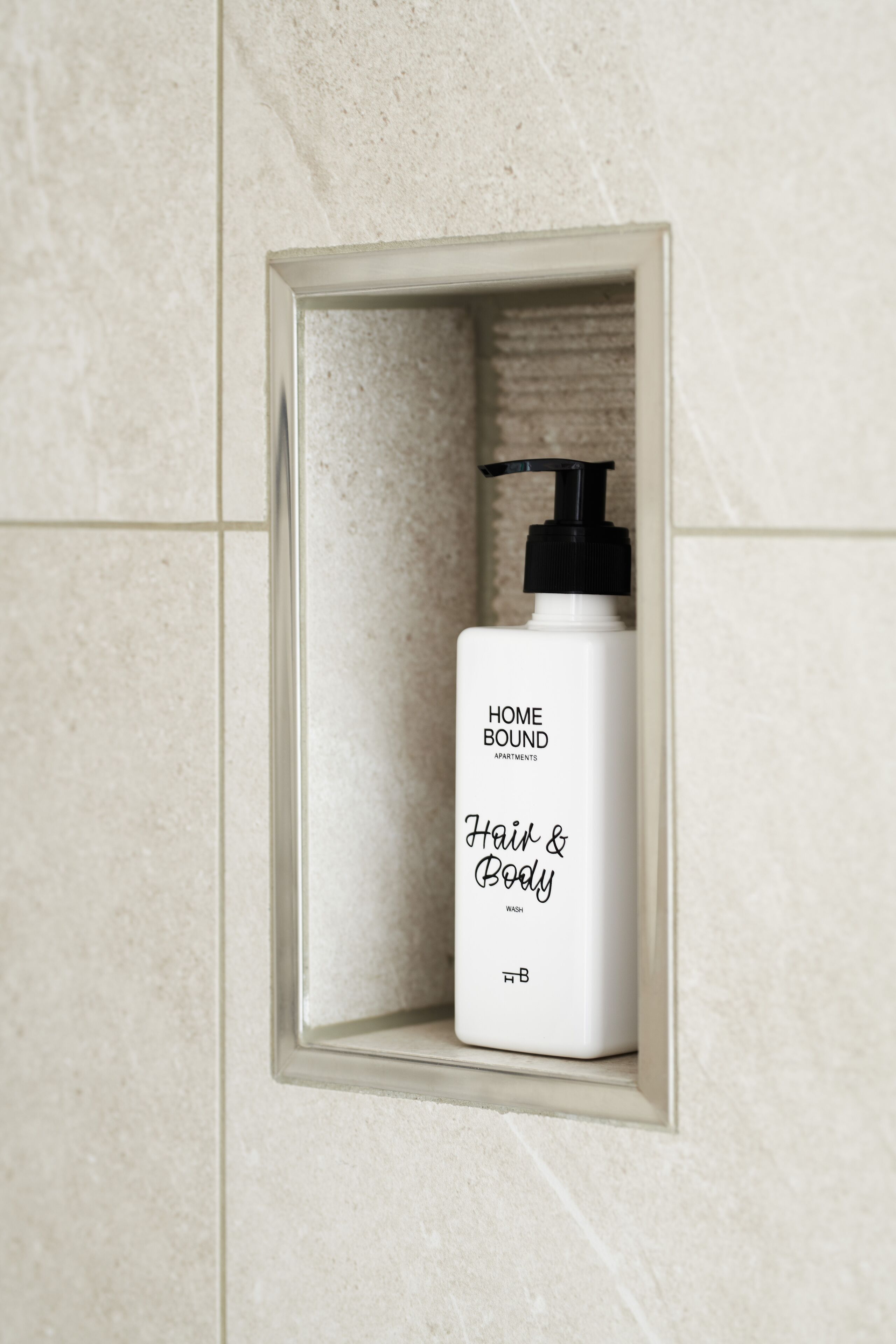 A bathroom with a white bottle of hair and body wash in a framed shelf.