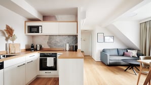 A modern kitchen with white cabinets, a microwave, and a stove. There is a dining area with a table and chairs, and a sofa with cushions.