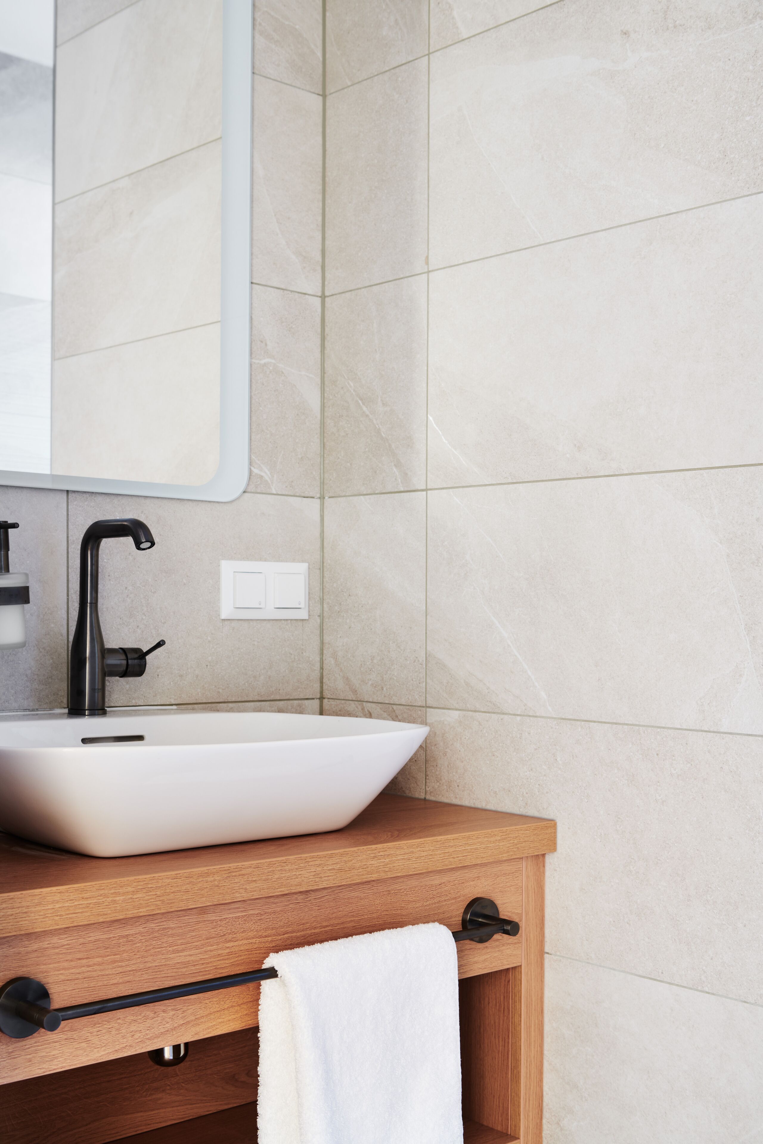 A bathroom with a white vessel sink, a wooden vanity, a black faucet, and a towel hanging on a rack.