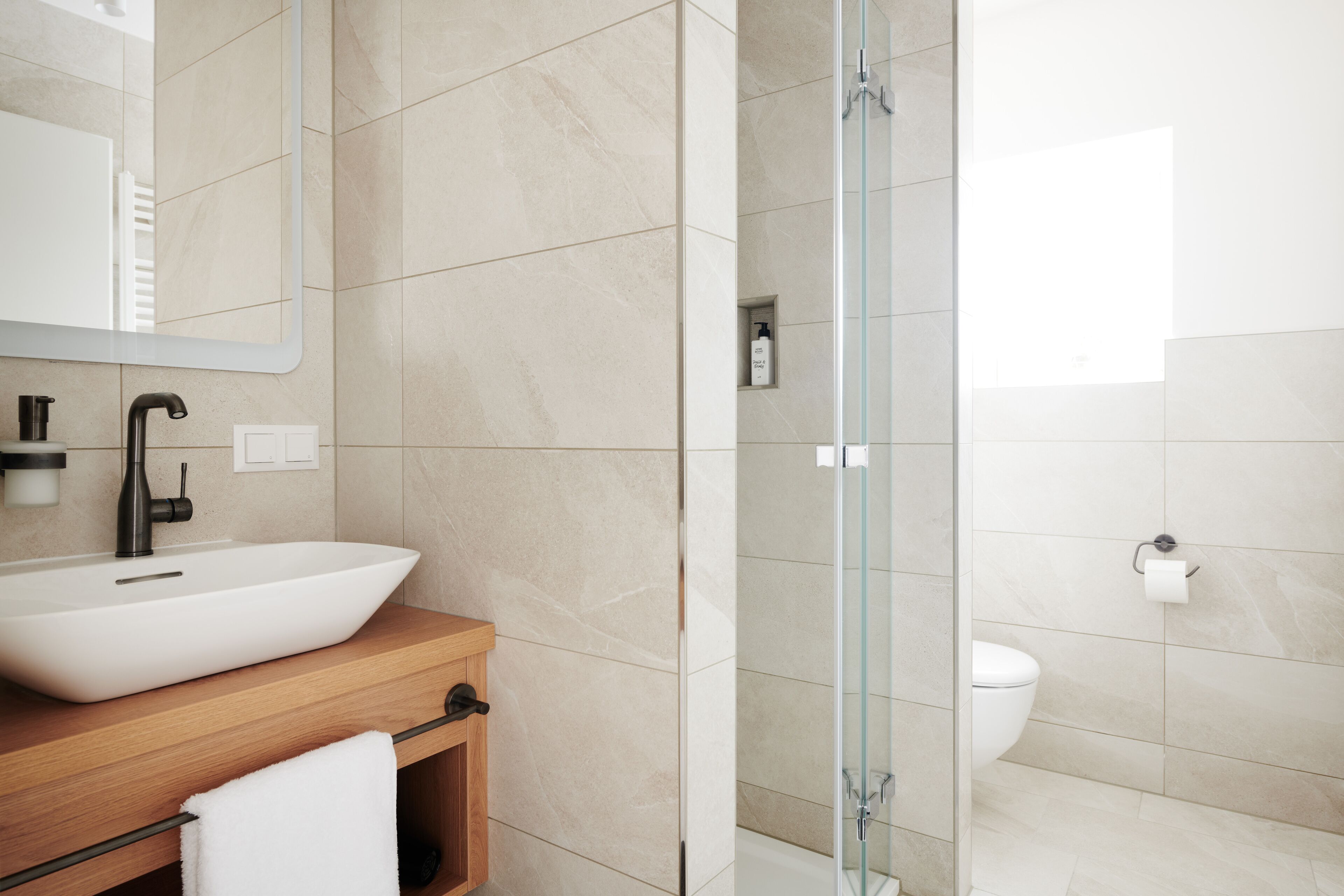 A modern bathroom with a large white sink, a wooden vanity, a glass shower enclosure, and a toilet.