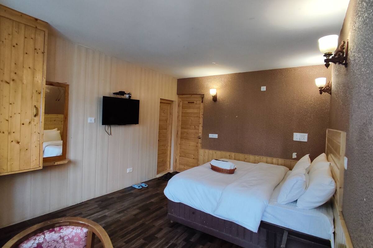 A room with a wooden bed, a television mounted on the wall, and a wooden wardrobe.