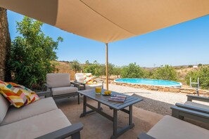 An outdoor patio with a pool, lounge chairs, and a table with drinks.