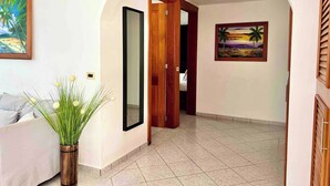 Ein Flur mit weißer Wand, einer Holztür, einem gerahmten Gemälde und einem Blumentopf.