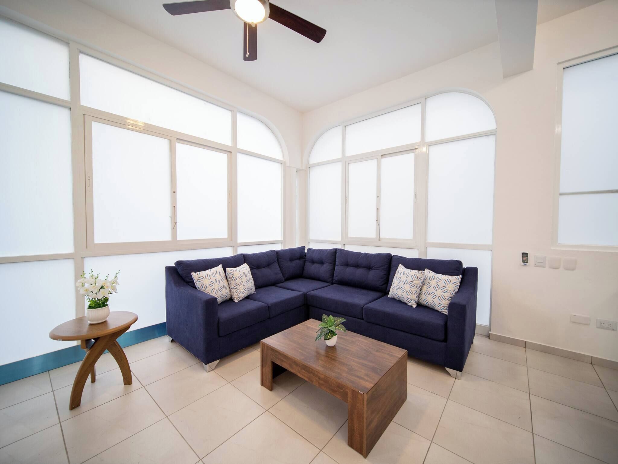 A room with a sectional sofa, a wooden coffee table, and a small round table with a plant.