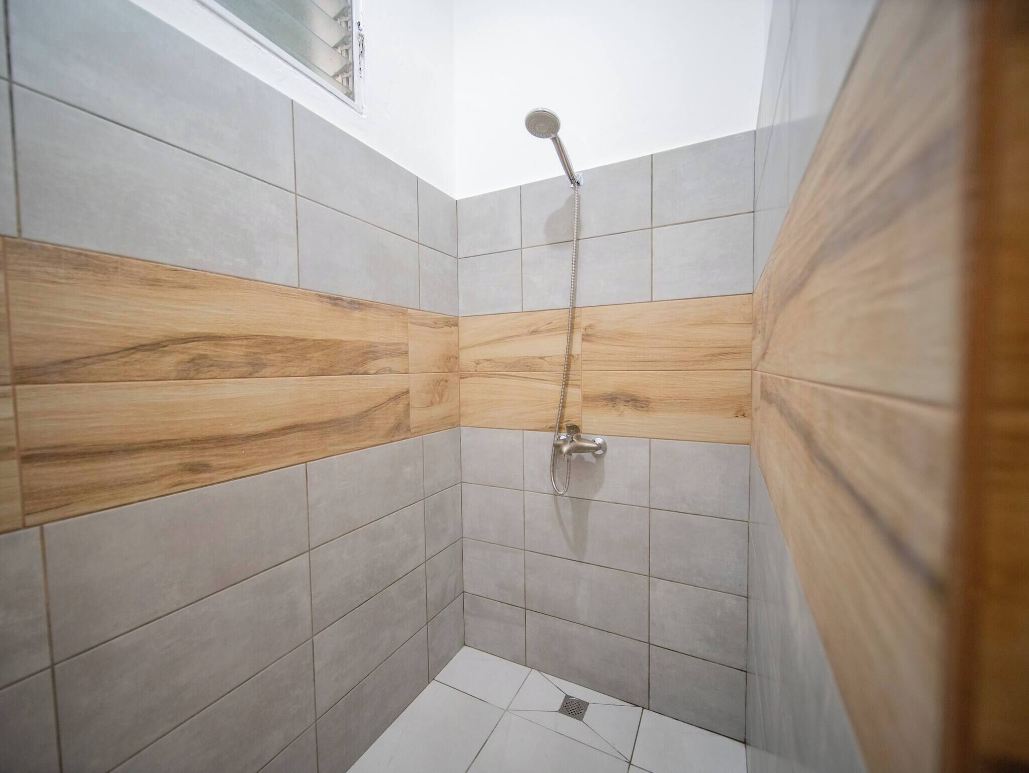 A shower with a handheld showerhead, tiled walls with a wood-like pattern, and a window above.