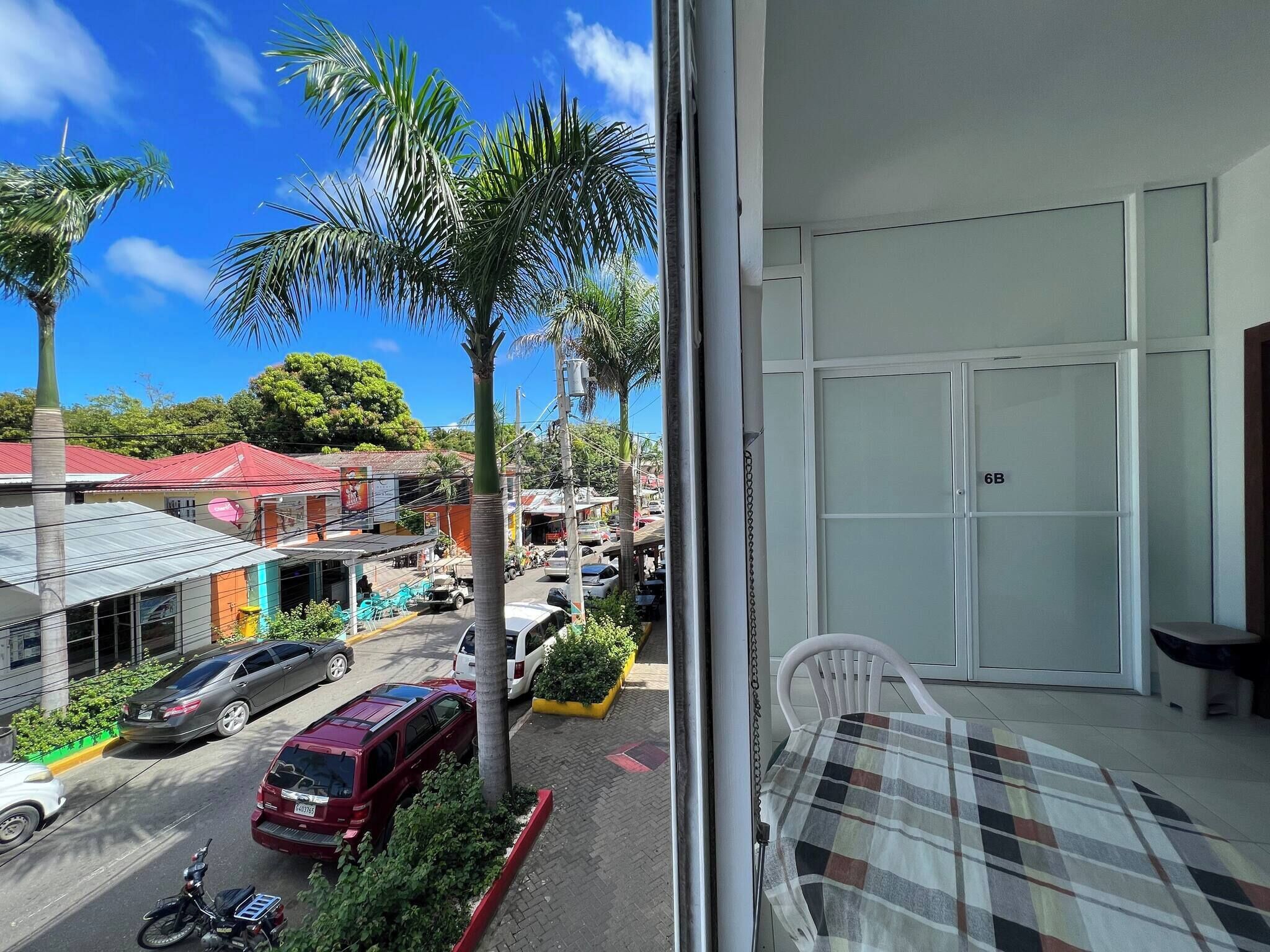 A hotel room with a large window overlooking a street with palm trees and parked cars.