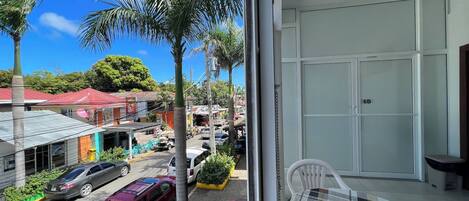 A hotel room with a large window overlooking a street with palm trees and parked cars.